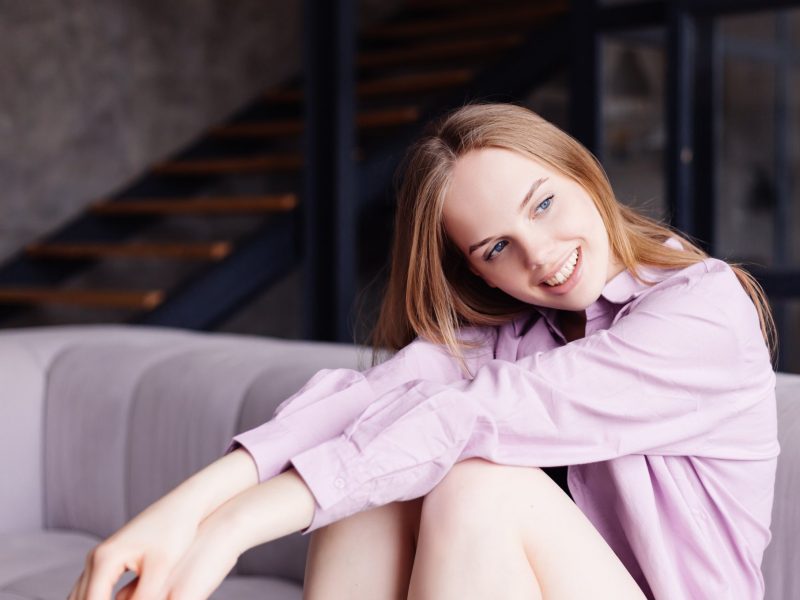 Young pretty girl in purple shirt on sofa cute and adorable smiling alone